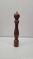 Front view of the full length wooden pepper grinder showing the tall, slim, turned wood design and narrow base.