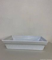Side view of white rectangular casserole dish showing ribbed exterior pattern and decorative upper edge.