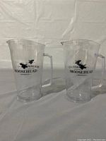 Two clear plastic Moosehead pitchers with black logo.