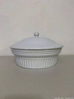 Side view of the white ceramic casserole dish with lid, showing textured band and ribbed lower pattern.