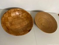 Photo showing both wooden woven bowl with square checkered pattern and circular textured bamboo bowl side by side on flat surface.