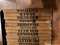 Spine view of 12 art books showing titles including Van Dyck, Rubens, Durer, Holbein, Murillo, Lawrence, Memling, Velazquez and others.