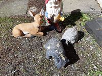 Four garden ornaments placed on ground: deer, bear, turtle, and gnome, showing wear and paint loss.