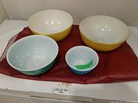 Photo showing all four bowls (2 large yellow, 1 medium aqua, 1 small blue) arranged on red cloth.