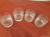 Four clear textured whiskey glasses displayed on orange surface, showing vertical ripple pattern and thick base.