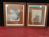 Pair of framed vintage etchings or prints shown side by side on a red surface with dark background.