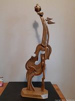 Front angled view of abstract wooden violin sculpture on wooden base, showing body and scroll details.