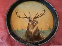 Top-down photo of round serving tray showing elk design on yellow background with black rim and wear.