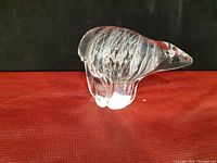 Front and side view of the blown glass polar bear figurine on a red surface with a black background.