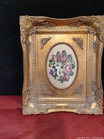 Full frontal view of the framed floral stitchery with ornate gold frame.
