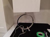 Full view of the vintage chrome table lamp with white rectangular shade on black surface against a beige wall.