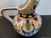 Side view of the pitcher showing detailed polychrome floral and scroll decoration and the handle design.