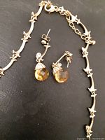 Close up of necklace and earring showing amber glass pendants and detailed gold-tone chain links and earring backs