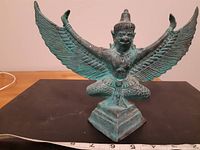 Full frontal shot of the bronze Garuda statue showing extended wings on a square base.