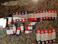 Top-down image showing 21 sealed Kem Glow color tinting tubes in original packaging laid out on a countertop showing various boxes mostly in red, blue, and white colors.