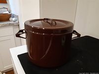 Side view of dark brown enamel pot with lid and side handles on black surface in kitchen setting.