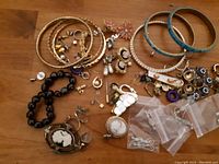 Photo of assorted vintage costume jewellery laid out on wooden surface, including bangles, brooches, clip earrings, and bracelets