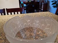 Clear and frosted crystal bowl with etched elephants visible around the top edge, placed on countertop in a room with chairs in background.