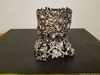 Side view of ornate antique metal wine bottle holder showing grapevine and leaf detailing with heavy tarnish.