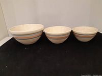 Front view of three nested vintage stoneware mixing bowls with concentric stripes in beige, blue, and orange.