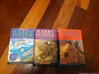 Photo showing all three Harry Potter books standing upright on wooden floor: Chamber of Secrets, Prisoner of Azkaban, Goblet of Fire