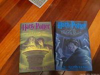Two hardcover Harry Potter books on a wooden floor, showing the front covers: 'Half-Blood Prince' and 'Order of the Phoenix'.