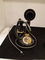 Front and side view of black and gold candlestick rotary phone with coiled handset cord and grey line cord
