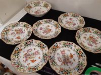 Seven dessert plates and one bowl arranged on table showing floral and gold decorative border