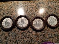 Four vintage circular wooden framed monochrome illustrations displayed in a row on a granite surface.
