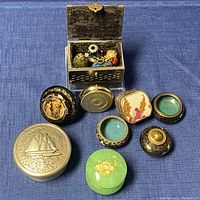Overall view of assorted vintage trinket boxes, cloisonné enamel salt and pepper shakers, salt cellars and miniatures displayed on blue fabric.
