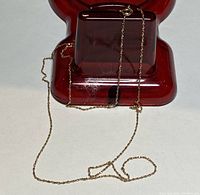 Gold chain necklace displayed on a red stand showing the chain's delicate link design and clasp.