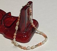 Full bracelet displayed on a red stand, showing pearls, coral beads and gold beads.