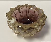 Angled view showing the ribbed and scalloped form, purple inner layer, and gold flecks in the clear glass body.