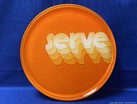 Top view of orange circular serving tray with 'serve' pop art text in white and yellow shades on the surface.