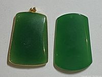 Two green jade pendants, one framed in gold-tone metal with bail, the other plain jade, front view