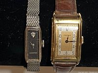 Two ladies windup watches side by side on black background, showing Longines watch with mesh metal band and another watch with brown leather strap and gold-tone rectangular case.