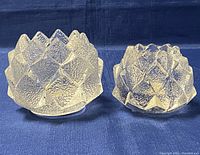Photo showing two frosted crystal candleholders with textured geometric design on a blue fabric background.