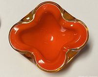 Top-down view of single ashtray showing bright orange interior and quatrefoil shape