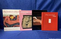 Four vintage erotic art books upright on blue fabric backdrop, titles visible and spines facing right.