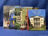 Five hardcover interior design and architecture books arranged side by side with covers visible on a blue fabric background.