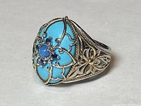 Angled side view showing turquoise inlay bordered by silver with filigree band details.