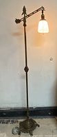 Full view of the antique bridge floor lamp lit, showing the cast iron base and adjustable arm with glass shade.