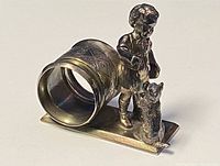 Side perspective showing the napkin ring cylindrical area with floral engravings next to the child and cat figurine on a rectangular base.