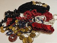 Multiple assorted necklaces with black, red, white, brown and blue beads in various shapes and materials