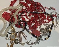 Overview photo showing assorted necklaces in red, black, white, and gold-tone, plus gold-tone watch and various decorative elements.