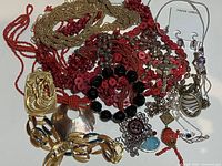 Photo showing an assortment of costume jewelry pieces with various beads, chains, and pendants laid out together.