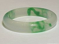 Top down view of a polished jade bangle bracelet showing green marbling on a light translucent base.