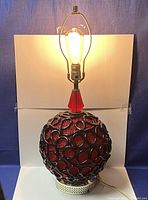 Side view of the spherical red lucite lamp with black spun ribbon overlay, showing lit bulb at top.