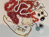 Top view of assorted vintage costume jewelry including colorful chip bead necklaces, clip-on earrings, gold-tone chain bracelet, and Lauren by Ralph Lauren black stone earring and necklace set.