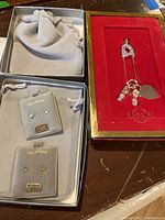 Two small velvet pouches containing two pairs of 14 KT gold baby girl stud earrings, and a red velvet box with gold trim housing the baby boy Lenox keepsake ornament shaped like a safety pin with dangling charms.